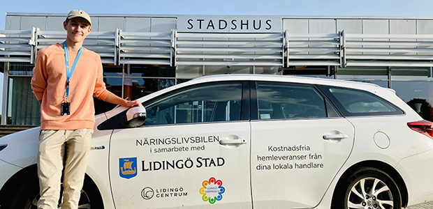 Kvinna står bredvid en vit bil i Lidingö centrum.