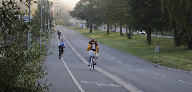 Gång och cykelbana med cyklister, bredvid en bilväg, träd och flaggor