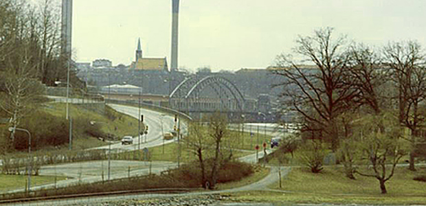Lidingö brostrand vid Islinge hamnväg, vid vattnet till höger i bild med Gamla Lidingöbron och Lilla Värtan i bakgrunden.
