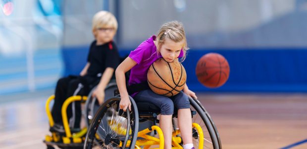 En flicka och en pojke i rullstol spelar basket.
