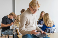 Elever i klassrum med laptops och mobiler.