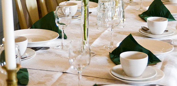 Bild på ett dukat bord med tallrikar, glas, blommor och ljusstakar.