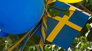 Svensk flagga, ballong och gulblått band björklöv.