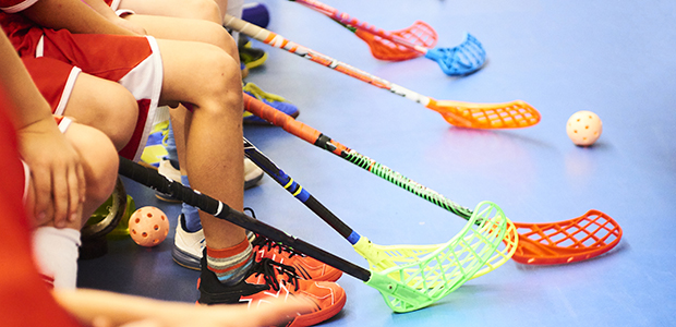 Barn sitter och väntar på att få spela innebandy. Färgglada klubbor på rad.