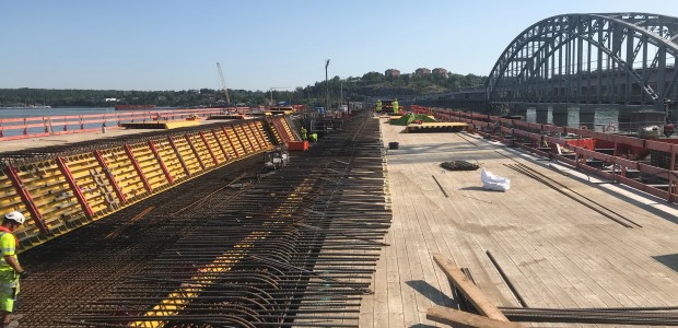 Träform och armering i den nya brokonstruktionen, bågspannet av den gamla bron, vattnet samt träd på Lidingö skymtar i bakgrunden.