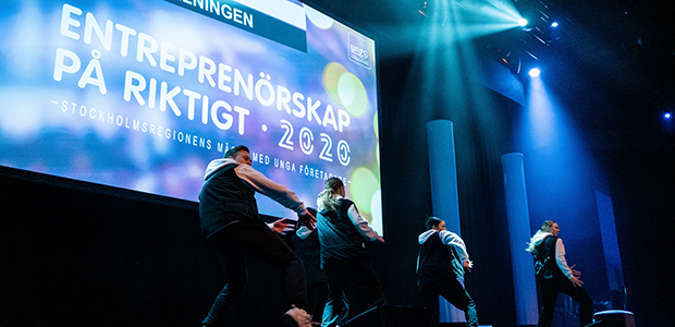 Dansande elever i ett mörkt rum framför en stor skylt där det står Entreprenörskap på riktigt 2020.