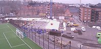 Byggarbetsplats med skymt av en fotbollsplan och tegelhus.